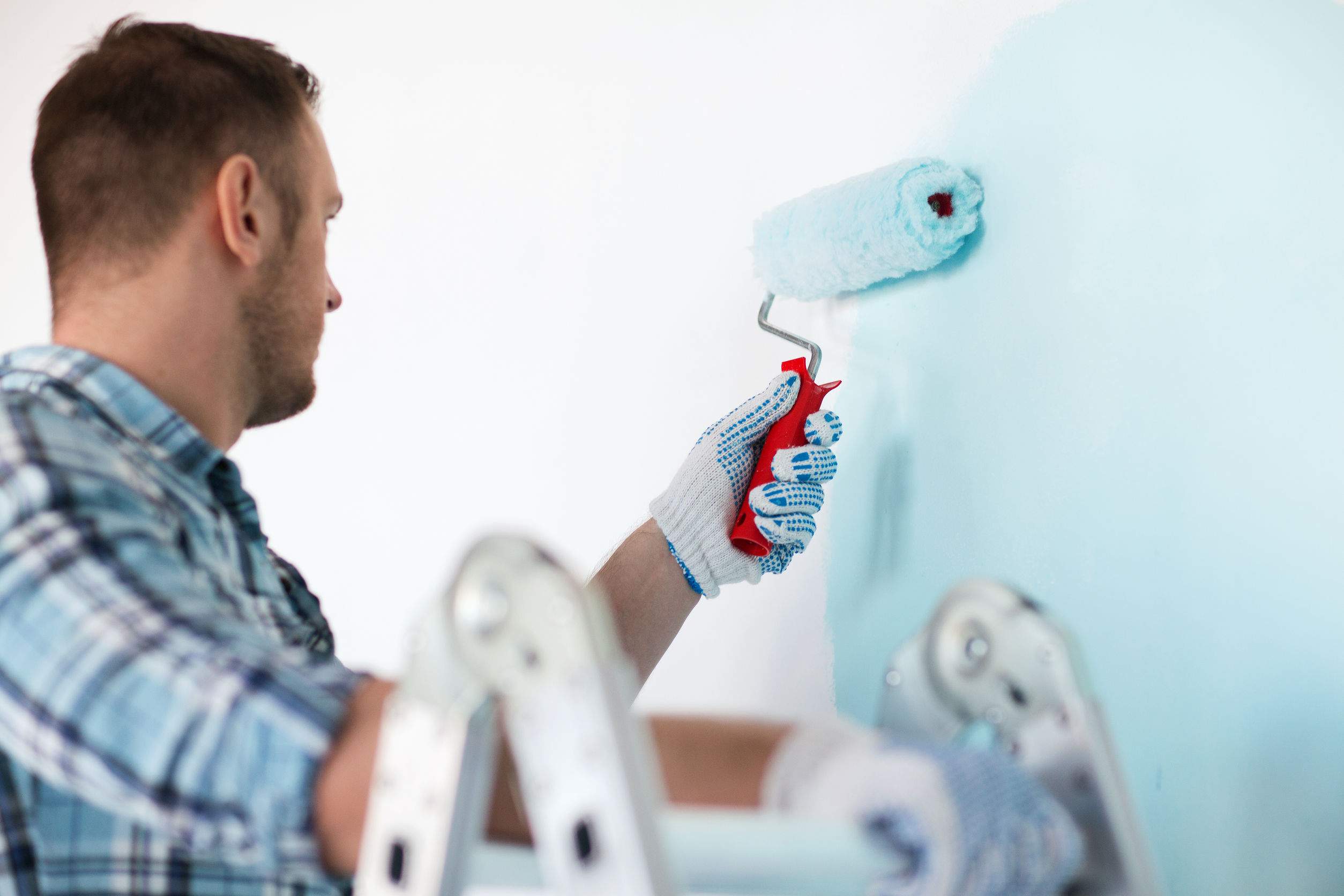 homme sur une échelle qui peint un mur au rouleau